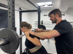 coach adjusts the squat bar position for a lifter